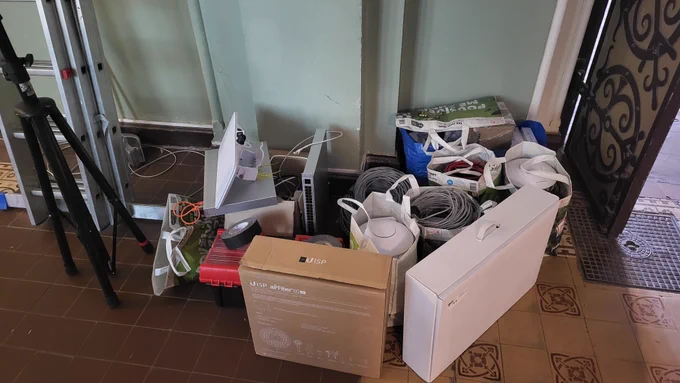 Pile of hardware from previous photo and other stuff packed into bags and boxes on a floor. The box in front has AirFiber 60LR inside, which was used for uplink to the venue. 