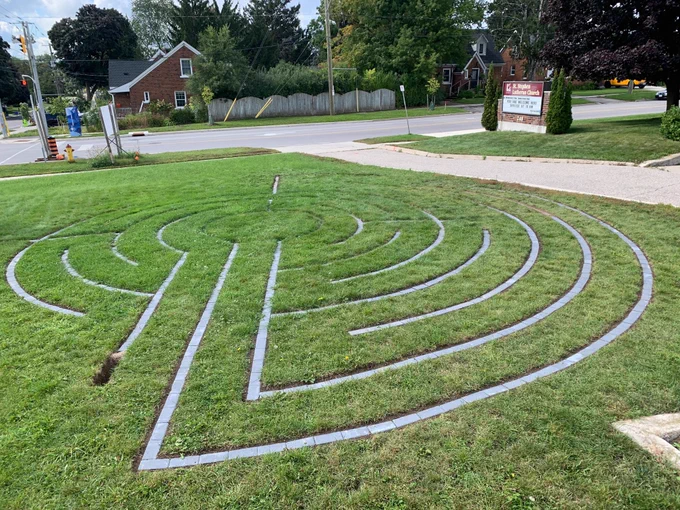 A circular labyrinth, made of paving stones set into a lawn, is being built. The area to the right is more developed, with the back and left needing more work.