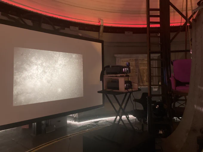 A picture of the "Her Luminous Distance" exhibition, showing a photo of a starry sky being projected onto the screen. This exhibition is inside the dome of the Great Refractor, a telescope at Harvard's Astrophysics Center.