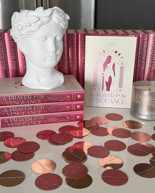 Stacks of my book with a shiny garland, candle, and plaster bust of an girl