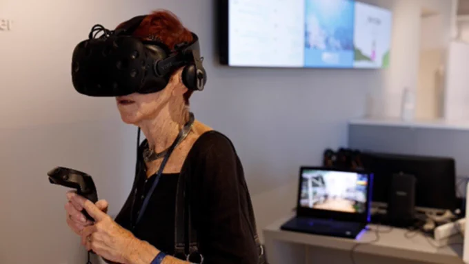 Woman wearing a Virtual Reality headset with a laptop in the background. 