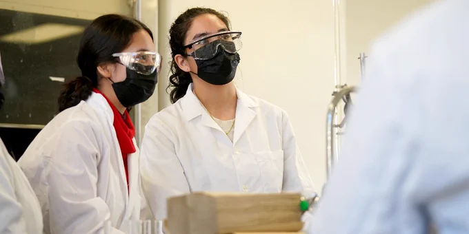 Two students in lab coats and safety goggles. 