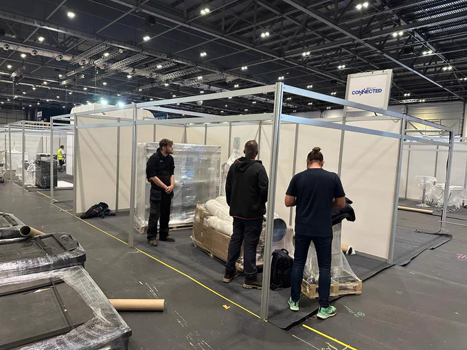three men at an empty stand with palleted goods on the floor