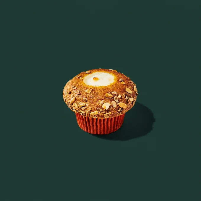 A pumpkin muffin with pepita seeds on top and a cream cheese center against a dark green background.