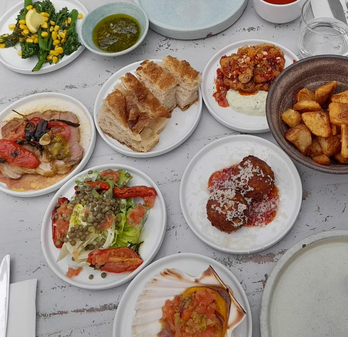 Picture showing eight different dishes of delicious food, including bread, broccoli, pork, chicken, fried potatoes and salad on a white table