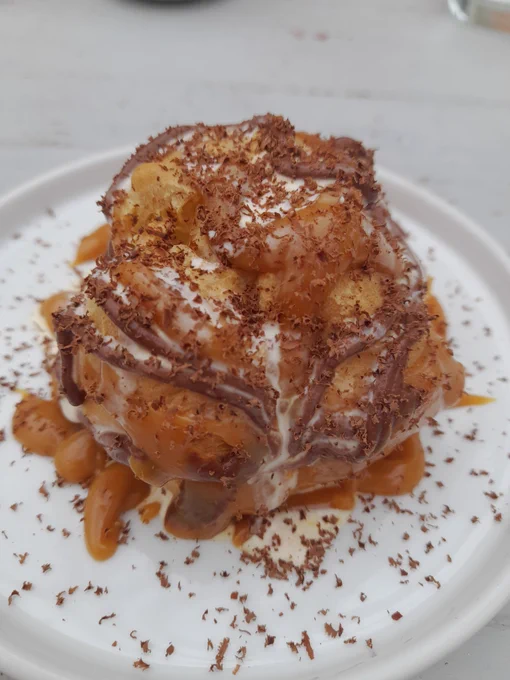 Picture of a tasty choux bun, filled with cream and ice cream, drizzled with caramel and chocolate sauce and grated chocolate