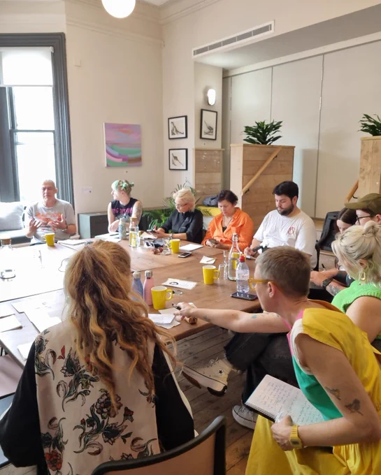 A group sit around a large table in a bright meeting room. 