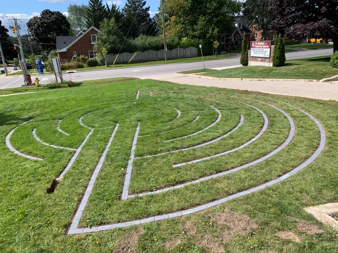 A circular labyrinth, made of paving stones set into a lawn, is being built. The area to the right is finished, and the left needs more work.