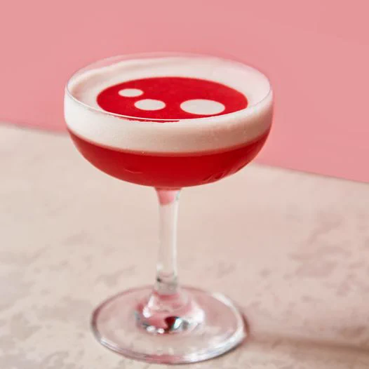 A bright red cocktail in a glass with white foam on top