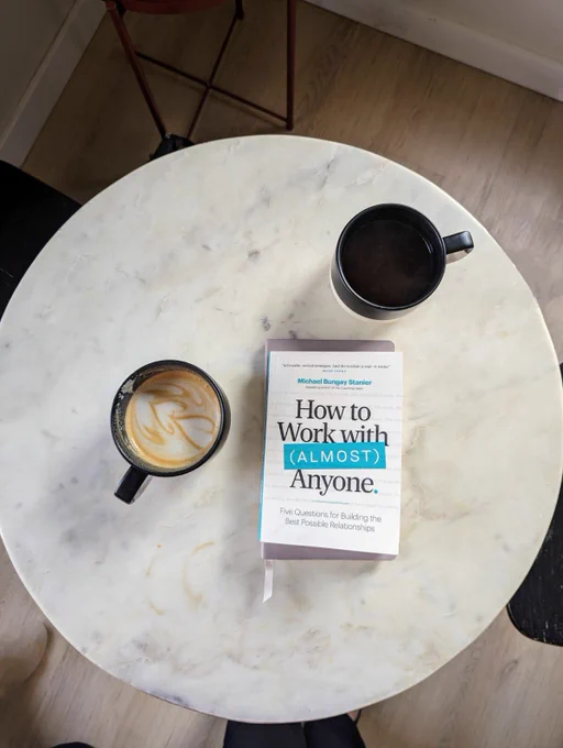 overhead view of a cafe table with 2 coffee mugs and the book "How to Work with "Almost" Anyone"