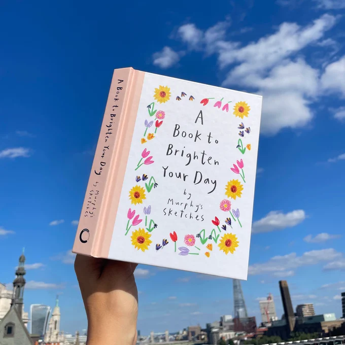A Book to Brighten Your Day held up against a blue sky