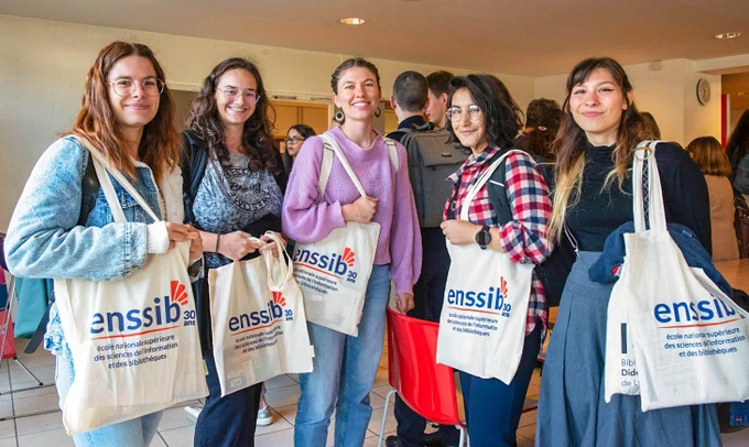 5 étudiantes en master de l'Enssib situées côte à côte (avec le sac estampillé "Enssib" distribué à l'occasion de la rentrée), lors de journée d'accueil des masters