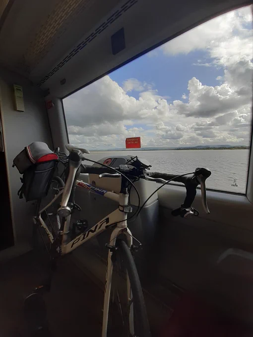 A white road bicycle is on a train passing alongside the River Severn towards Gloucester. 