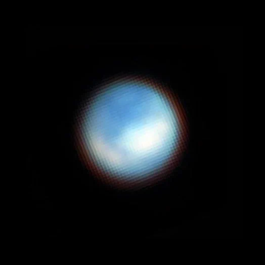 A blue-and-white sphere against a black background is somewhat reminiscent of the famous “Blue Marble” picture of Earth from space. With fuzzy, diffuse edges, this sphere features darker blue patches in most of the northern hemisphere facing the viewer. One, large, crescent-shaped, white patch extends along the left side of the southern hemisphere facing the viewer, and a larger, blobby, white patch covers the middle latitudes of the right side of the southern hemisphere. Lighter blue regions border these white patches in the south.