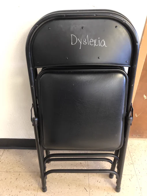 A black folding chair that says dyslexia in white paint on the top
