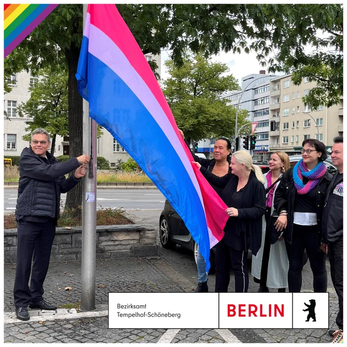 Ein Mann hisst gemeinsam mit weiteren Personen die Bi-Flagge