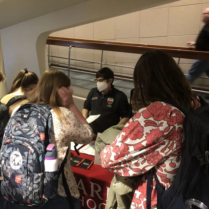 Students cluster around a table covered with library information while an HLS Library staff member chats with them while standing behind the table.