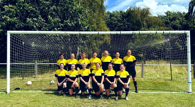 The HIWFRS women's football team line up for a photo in their football kit in front of a goal