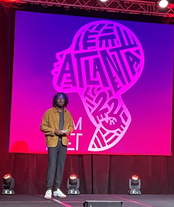 Mikhael Simmonds, Executive Director at the Center for Community Media at CUNY, on stage with the ComNet23 Atlanta logo on the back wall.