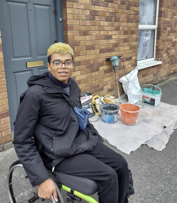 A person in a wheelchair next to a path that is partially blocked with building supplies.