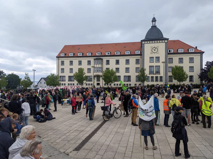 Vor dem Rathaus in Sassnitz steht eine Menschenmenge auf dem Platz. Einige davon halten Banner und Schilder.