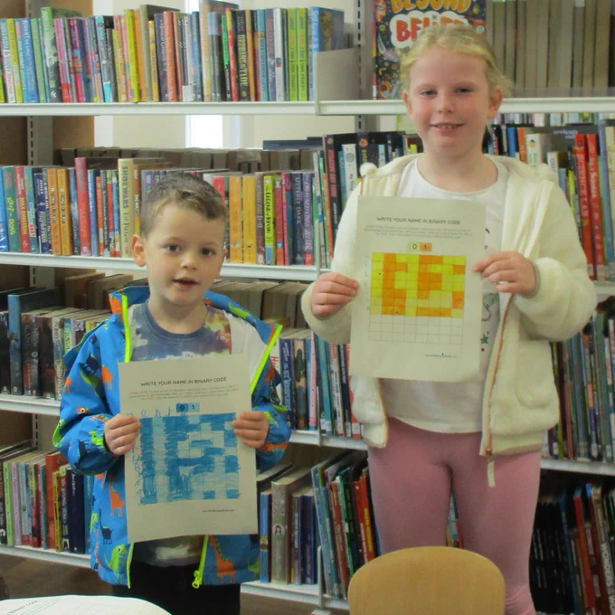 two children holding papers showing their names in binary