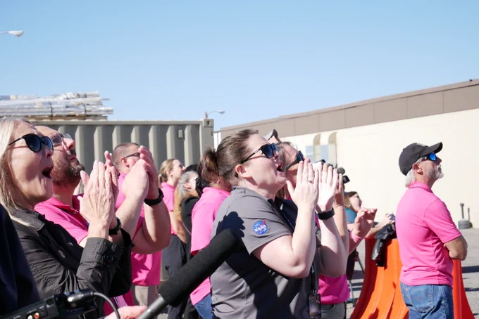 A group of people stands outside and claps and cheers. 