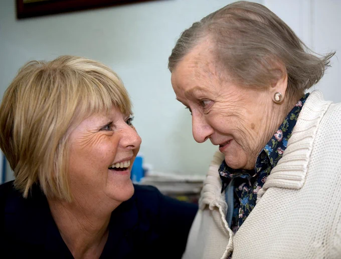 A care worker and an elderly woman smiling at each other