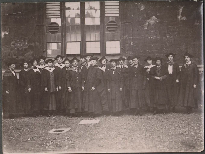 Black and white photo of some of the first women graduates in academic gowns.

