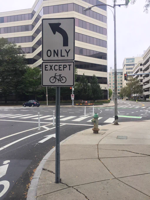 Bike lane approaching a signalized intersection with a sign depicting “Left turn only except bikes”.
