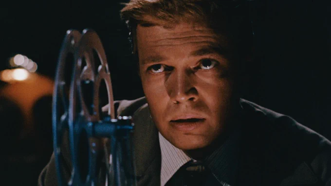 A close-up on a man with his face close to an empty film reel. 