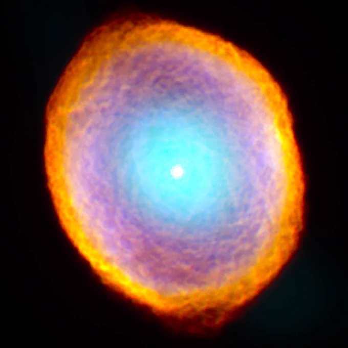 This nebula resembles a geode — a rock which reveals layers of colorful crystals when cut open. At the Spirograph's core is a small, bright white dot that's surrounded by a sky-blue glow. Encircling the glow is a thick ring of purple, marbled with faint orange lines that resemble tightly-tufted clouds. Around the purple ring, there is yet another ring with cloud-like texture, this time in bright orange and outlined with a fine red outer edge.