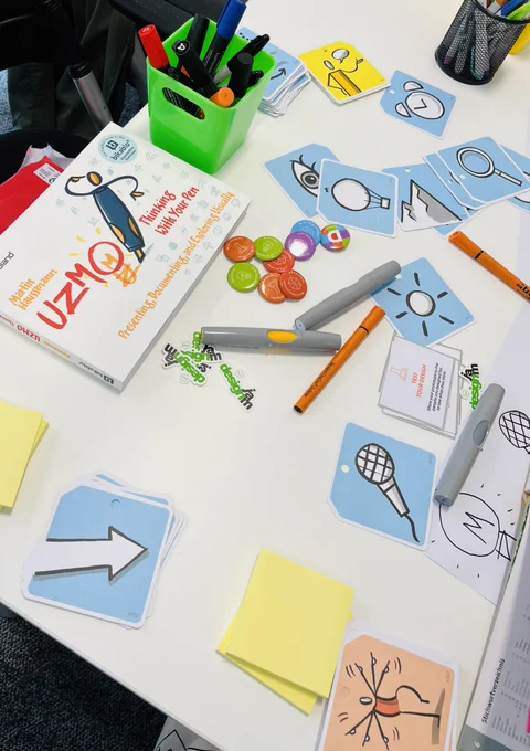 Table with stickers, badges, pens and bikablo cards with icons and people on.