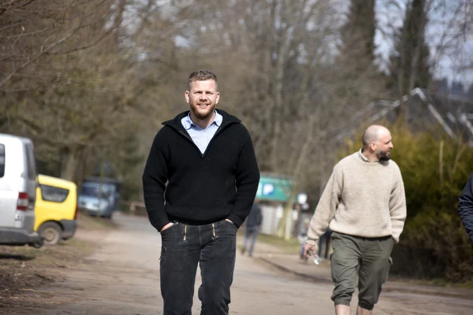 Das Bild zeigt Marcel Wöll aus Hessen auf dem Artgemeinschaftstreffen im März 2022. Er trägt ein hellblaues Hemd, einen schwarzen Pullover und eine schwarze Zimmermannshose. Bildrechte Exif-Recherche