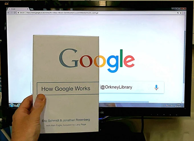 A monitor displaying Google with a copy of How Google Works in front of it