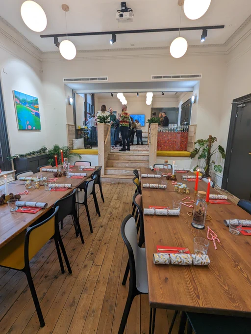 A room set up for a Christmas Dinner, people are networking in a separate area. 