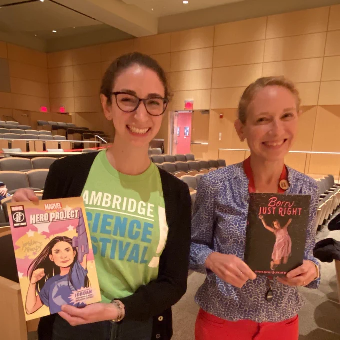 Two women stand together smiling. One holds a comic book and one holds a copy of the Born Just Right book.