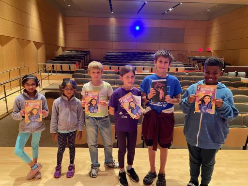Kids line up on a stage holding comic books