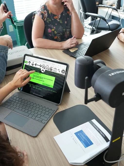 Finger points to a laptop screen with magnified material on it. The MagniBot sits beside.