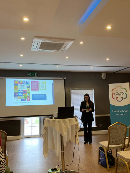 Woman talking to a room of people in front of a screen with a PowerPoint