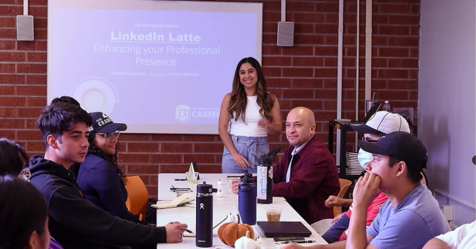 A person stands in front of a table of students presenting about the LinkedIn networking platform.
