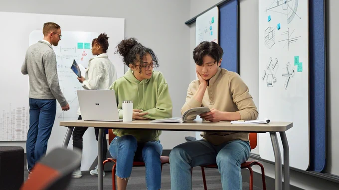 Two college students collaborate in red Elbrook chairs at a Steelcase Agree Table in an active learning classroom.