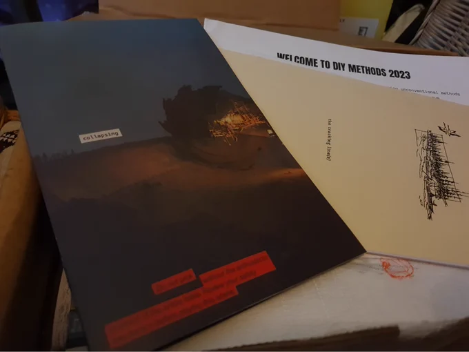 photo of a box full of different zines and a "welcome to DIY Methods 2023" note with a zine about collapsing sitting on top.