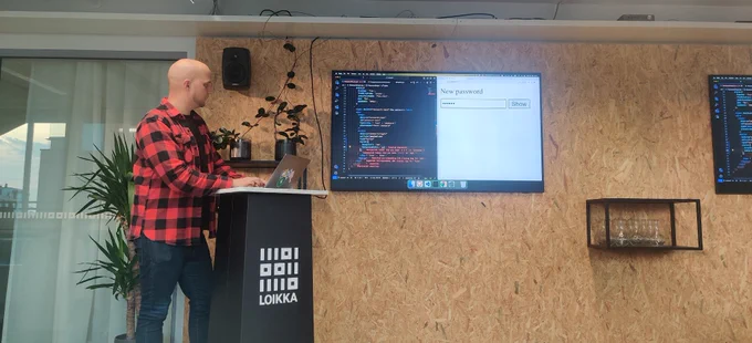 Ari doing a live demo with a code editor and browser open on a large screen while he stands next to a laptop stand.