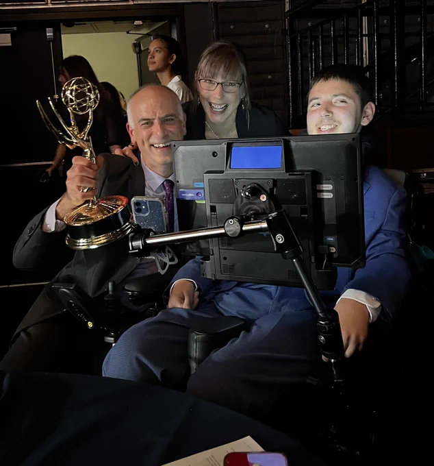 Dan, holding an Emmy award, with Samuel, and Betsy. They are all smiling.