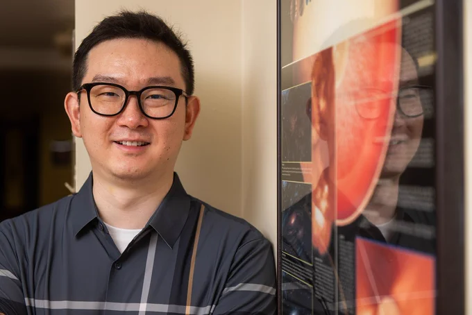 Chuanfei Dong (an East Asian man in a polo shirt) standing next to a poster of the sun
