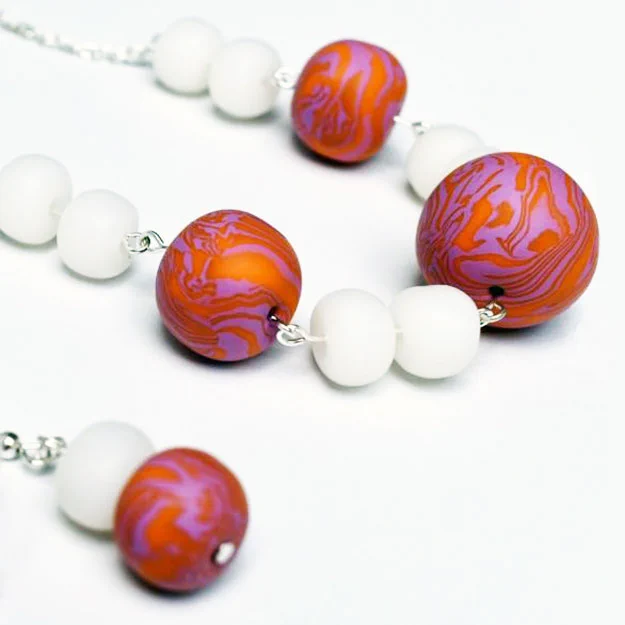 a necklace and earring made from polymer clay in white or marbled red and pink beads.