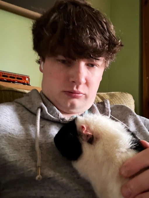 A selfie, featuring a black and white fuzzy guinea pig perching on James’s chest.