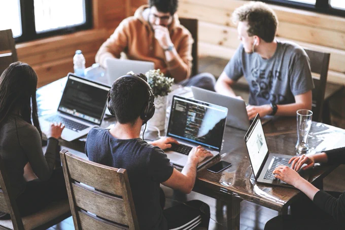 eine Gruppe von Menschen, die um einen Tisch mit Laptops sitzen.