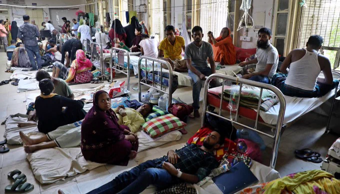 People sit and lay on beds with others on the floor in an overcrowded hospital in Bangladesh. Some look at the camera, while others sleep. 
